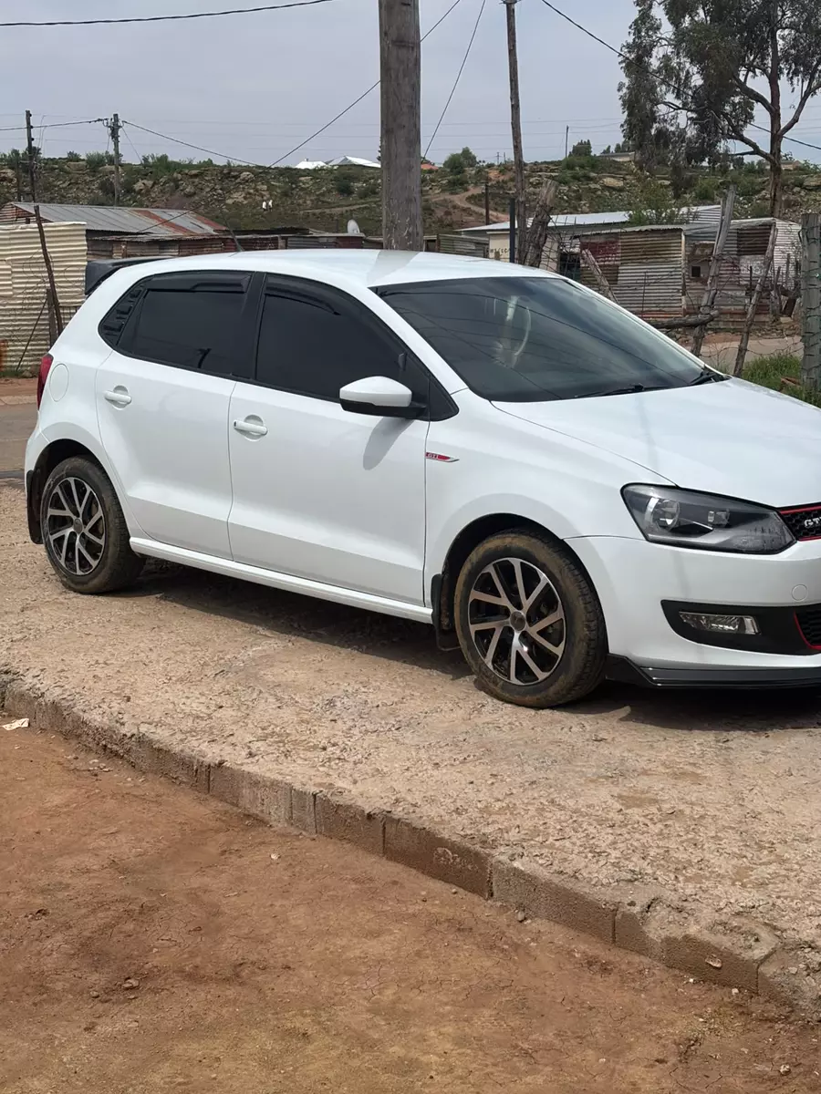 White hatchback parked on a dirt road in a residential area