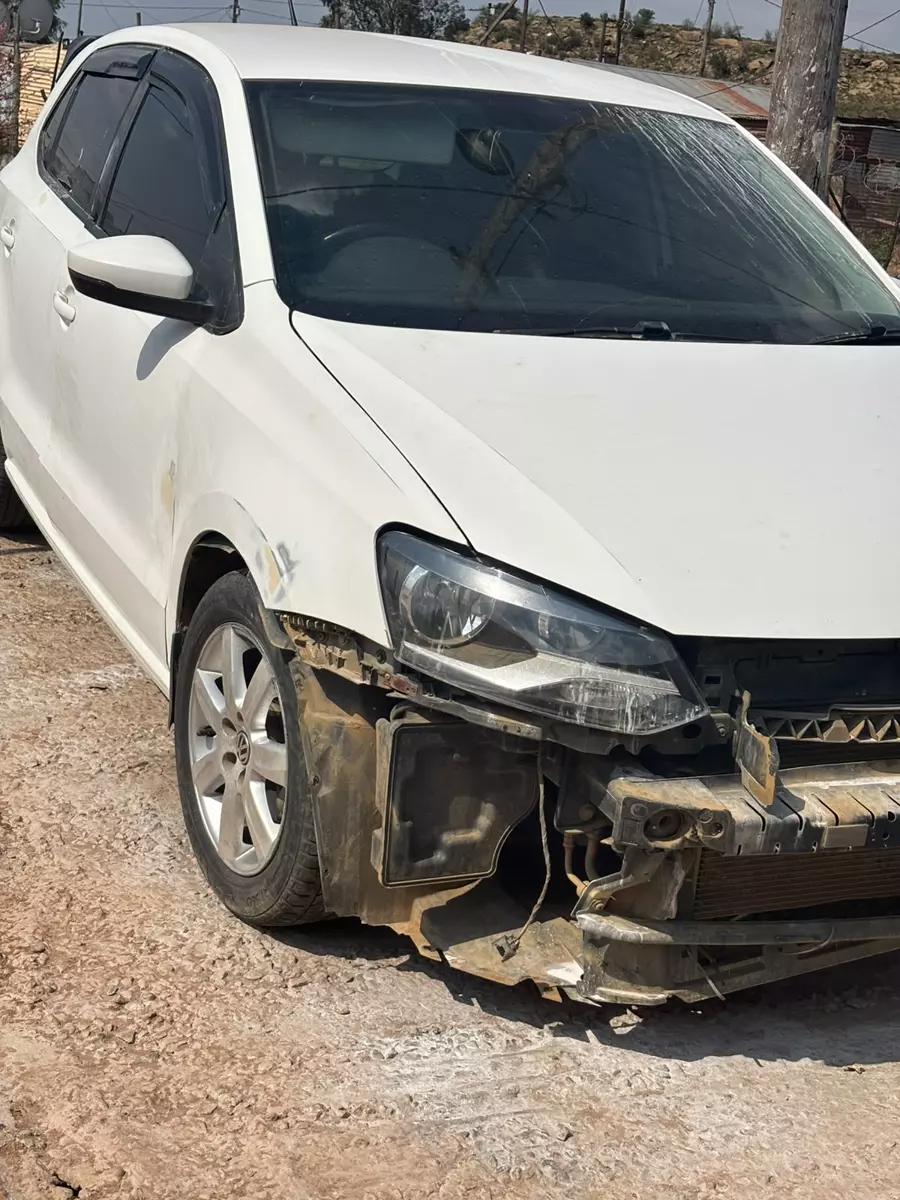 Damaged white hatchback parked on dirt ground before repairs