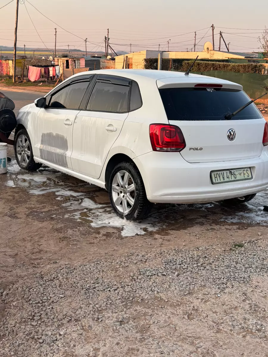 A white Volkswagen Polo being washed on a gravel street