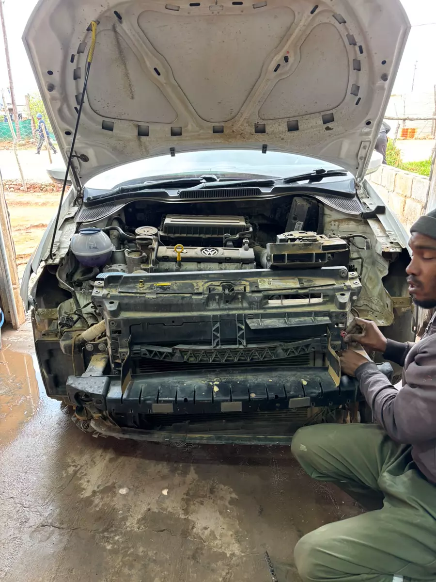 A mechanic working on the front of a white car with the hood open